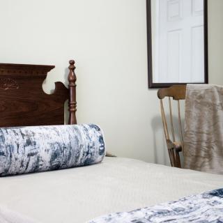 A cozy bedroom with a wooden headboard, a patterned pillow, and a chair beside the bed.