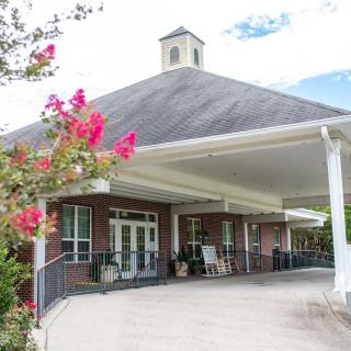 A building entrance with a covered porch surrounded by flowering plants.