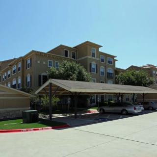 A multi-story apartment building with a carport and parked cars on a sunny day.
