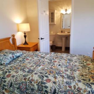 A cozy bedroom with a floral-patterned bedspread, wooden nightstand, and a view into an adjacent bathroom.