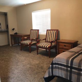 A cozy bedroom with striped chairs, a bed, and a desk under a window.