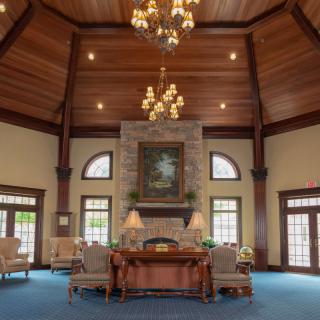 A spacious and elegant lobby with a high wooden ceiling, featuring chandeliers, comfortable furniture, and a fireplace.