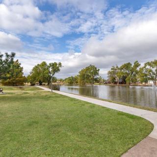 A serene park with a lake, grassy area, and a winding pathway under a cloudy sky.