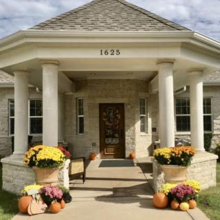 A welcoming porch decorated with flowers and pumpkins, showcasing a lovely stone house facade.