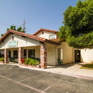 A small clinic with a tiled roof and stone columns, surrounded by trees and a parking lot.