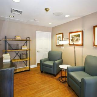 A cozy waiting room featuring comfortable armchairs, a shelving unit, and framed artwork on the walls.
