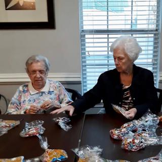 Two elderly women sitting at a table filled with candy.