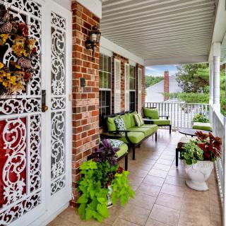 A cozy porch with green cushioned chairs, decorative ironwork, and vibrant plants.