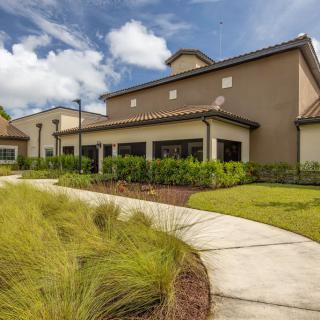 A modern building with a winding pathway surrounded by lush greenery under a cloudy sky.