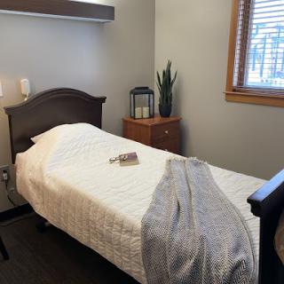 A simple and clean single bedroom with a neatly made bed, an indoor plant, and wooden furniture.