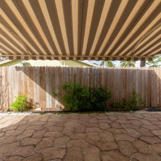 A patio with a striped awning providing shade, bordered by a wooden fence and stone flooring.