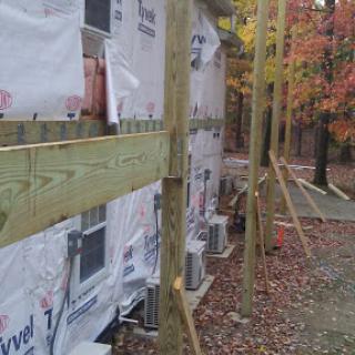 Construction site showing wooden supports and exterior walls covered in protective sheeting, surrounded by autumn foliage.