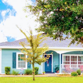 A charming blue house with a welcoming front porch and a small tree in the yard.