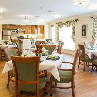 A well-lit dining room with arranged tables and chairs, featuring elegant decor and adjacent kitchen space.