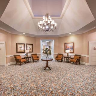 A beautifully decorated lobby area featuring elegant furniture, artwork on the walls, and a central table with a floral arrangement under a chandelier.