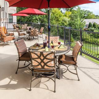 A sunny patio with a table, chairs, and a red umbrella overlooking a garden.