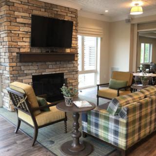A cozy living room with a brick fireplace, plaid sofa, armchairs, and a mounted television.