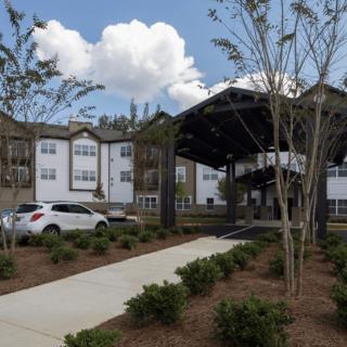 A modern building with a covered entrance, surrounded by trees and landscaping.