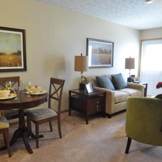 A cozy living and dining area featuring a comfortable sofa, elegant chairs, a round dining table, and tasteful artwork on the walls.