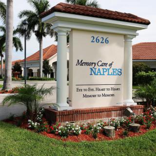 Entrance sign for a care facility surrounded by flowers and palm trees.