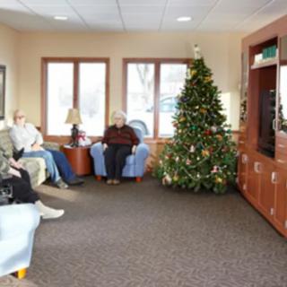 A cozy living room with a decorated Christmas tree and people sitting, watching television.