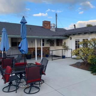 A cozy outdoor patio area with tables, chairs, and umbrellas against a building backdrop under a partly cloudy sky.