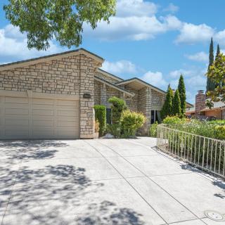 A suburban house with a large driveway and attached garage surrounded by trees and greenery.