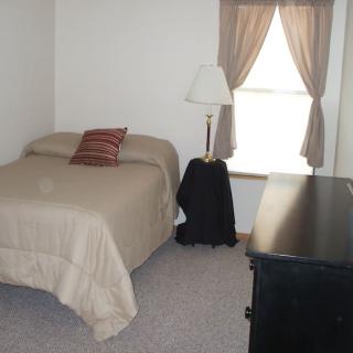 A simple bedroom with a bed, lamp, and dresser near a window with curtains.