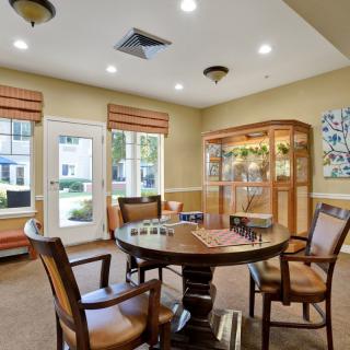 A cozy interior room featuring a round table and chairs, surrounded by windows and a display cabinet.