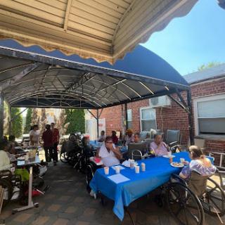 A cheerful outdoor gathering of seniors enjoying a meal together under a shaded area.