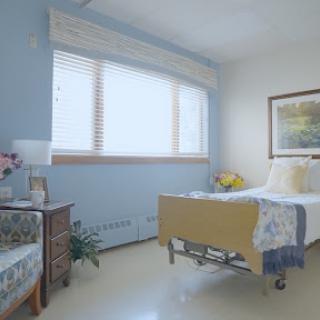 A bright and serene hospital patient room featuring a bed, a comfortable chair, and natural light streaming in through the window.