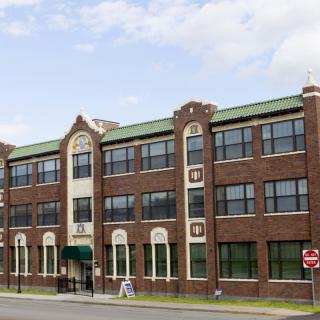 A three-story brick building with large windows on a city street under a cloudy sky.