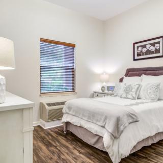 A cozy bedroom with a neatly made bed, nightstand, and soft lighting.