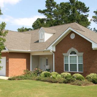 A suburban brick house with a well-maintained lawn and surrounding trees.