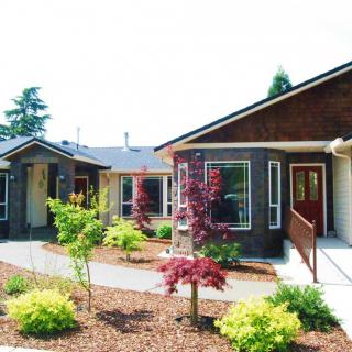 A view of single-story houses surrounded by landscaping, including trees and shrubs, under a clear daytime sky.