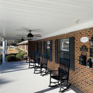 A porch with rocking chairs and ceiling fans along a brick wall.