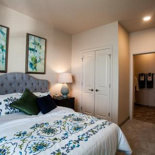 A cozy bedroom featuring a neatly made bed with patterned bedding, bedside table with a lamp, and artwork on the walls.
