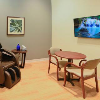 Relaxing waiting room with a massage chair, table, and television.