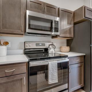 A modern kitchen with a stainless steel oven and microwave, surrounded by dark wooden cabinets.