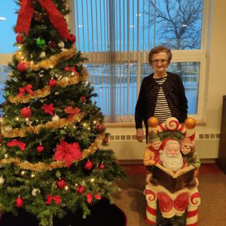 A person standing beside a decorated Christmas tree and a Santa figure indoors.