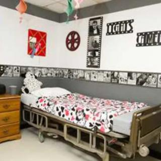 A movie-themed bedroom with a hospital bed, decorated with film reel posters and a dresser.