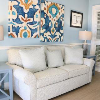 A cozy living room with a light-colored sofa, vibrant wall art, and matching lamps.