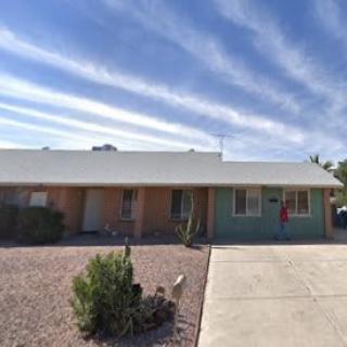 A single-story house with a xeriscaped front yard under a blue sky with streaked clouds.