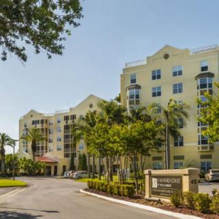 A sunny view of a residential condominium surrounded by palm trees and well-maintained landscaping.