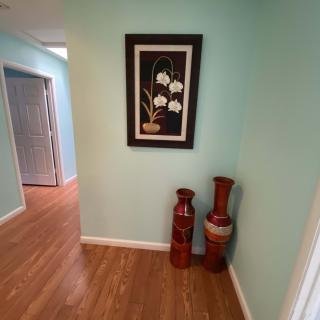 A hallway with a floral painting and two decorative vases on a wooden floor.