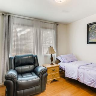 A cozy bedroom with a single bed, recliner, and natural light from large windows.