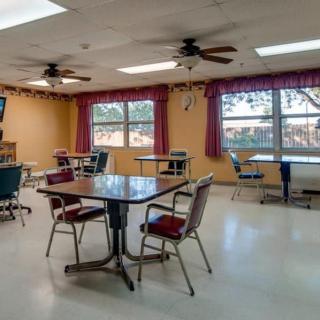 An empty dining area with tables and chairs, featuring large windows and ceiling fans.