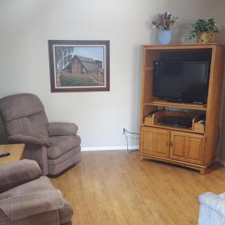 A cozy living room with a comfortable armchair, wooden cabinet, television, and a painting on the wall.