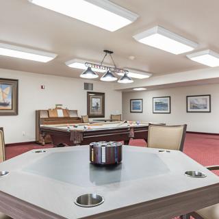 A recreation room featuring a pool table and poker table, with framed artwork and seating areas.