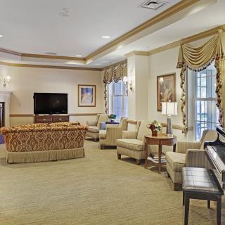 A cozy and elegantly furnished living room with comfortable seating, a piano, and a television.